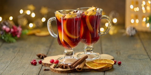 Dois copos de vinho quente com especiarias na montanha-russa de madeira. Bebida de Natal com canela, cardamomo, cravo, laranja, anis, cranberry. Foco seletivo, fundo desfocado, bokeh, horizontal, espaço de cópia