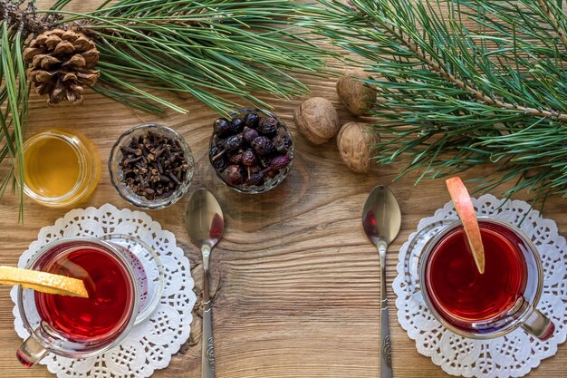 Dois copos de vinho quente com pedaços de canela em pau de laranja e anis estrelado de maçã sobre uma mesa de madeira