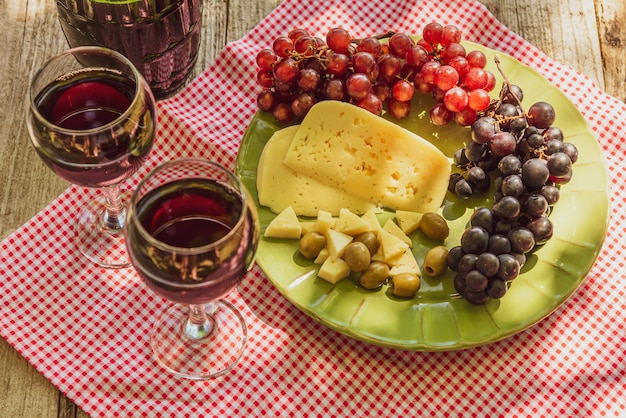 Dois copos de vinho tinto com um cacho de uvas, queijo e azeitonas.