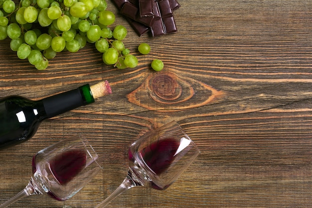 Dois copos, garrafa de vinho tinto e uva em uma mesa de madeira. vista do topo. copie o espaço. postura plana. natureza morta