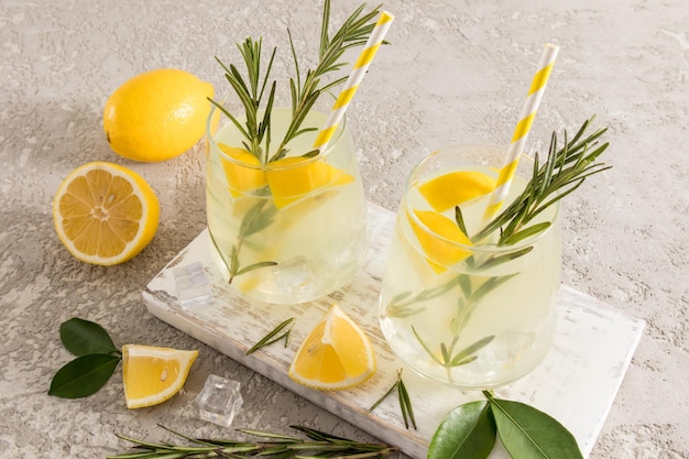 Dois copos grandes com limonada caseira refrigerada saudável em uma placa branca de madeira e uma mesa de concreto com alto teor de vitamina C