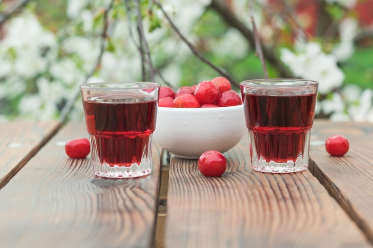 Foto dois copos pequenos com licor de cereja e frutas vermelhas sobre uma árvore em flor. álcool caseiro feito de frutas vermelhas.