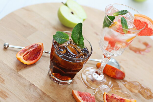 Dois coquetéis de uísque com cola e toranja com vodka com gelo e hortelã. em uma tábua de madeira, fragmentos de frutas são arremessados. foto com profundidade de campo.