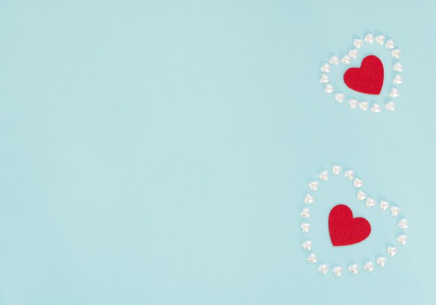 Dois corações de feltro vermelho dentro de um coração feito de pequenos corações de pérola sobre fundo azul. Dia dos namorados, casamento, amor, conceito de felicidade.