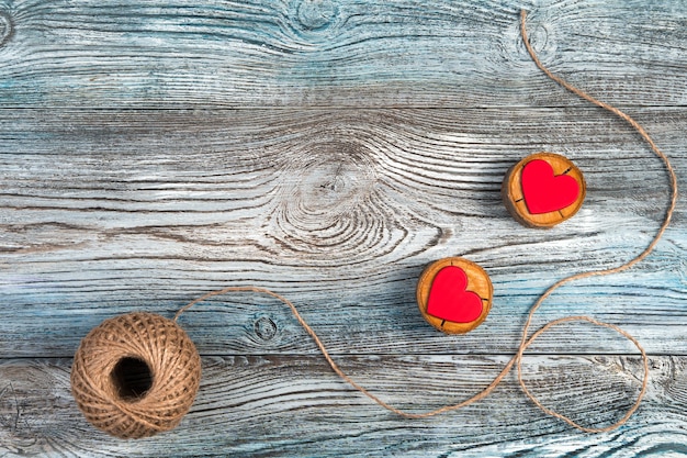 Dois corações vermelhos em suportes de madeira com fio de juta em um fundo cinza-azulado de madeira.
