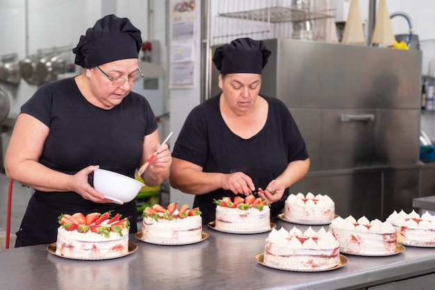 Dois cozinheiros chefe de pastelaria da mulher que trabalham junto fazendo bolos na loja de pastelaria.