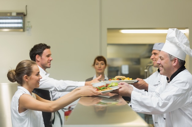 Dois cozinheiros que entregam pratos para servidores