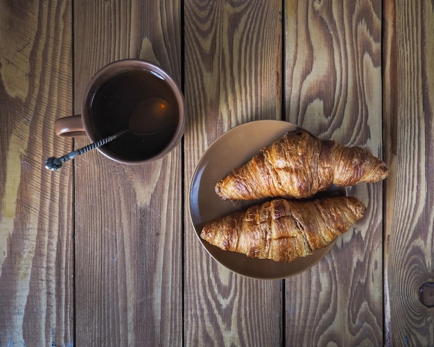 Dois croissants e uma xícara de chá em uma tigela marrom sobre uma mesa de madeira