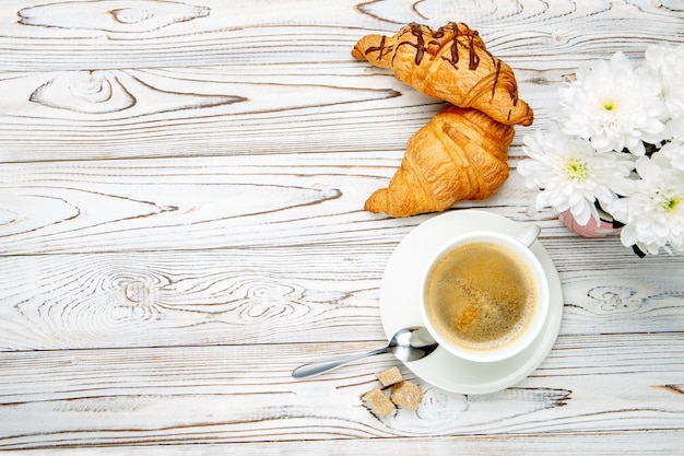 Dois croissants frescos e café, flores sobre fundo de madeira