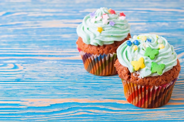 Dois cupcakes artesanais coloridos com creme verde sobre fundo azul de madeira.