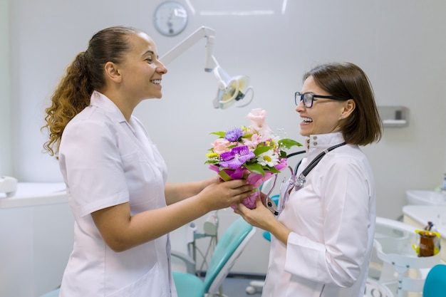 Dois dentistas femininos com um buquê de flores no consultório odontológico