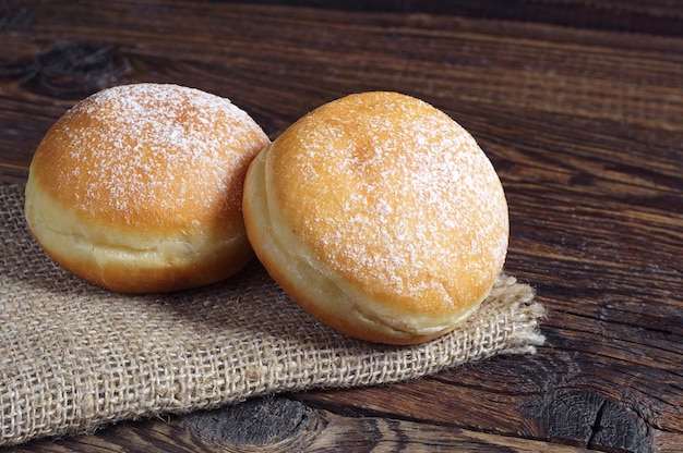 Dois donuts berliner com açúcar de confeiteiro na mesa de madeira
