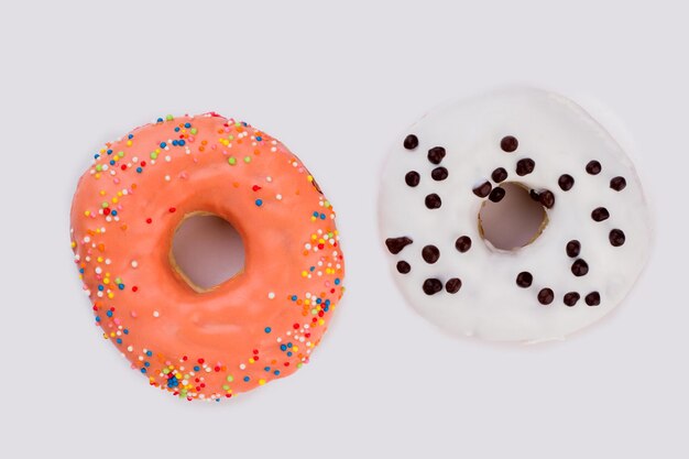 Dois donuts coloridos sobre fundo branco. rosquinhas laranja e brancas com granulado. sobremesa geada saborosa.