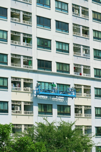 Dois dos trabalhadores de acesso por corda pintando a fachada de um edifício alto e moderno