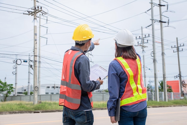 Dois eletricistas asiáticos na estação de sistema de energia de inspeção de serviço no local