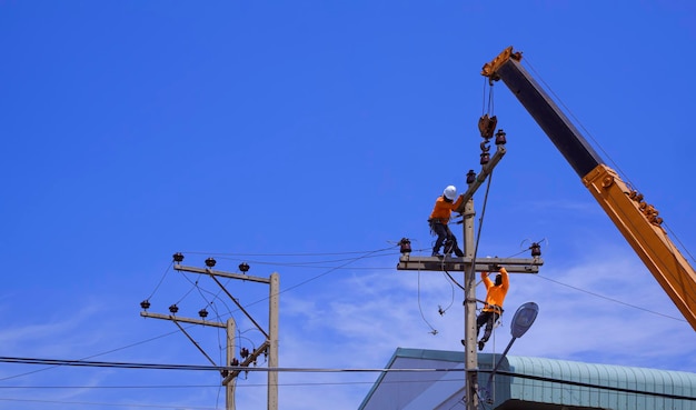 Dois eletricistas com caminhão guindaste instalando equipamentos elétricos no poste de energia contra o céu azul