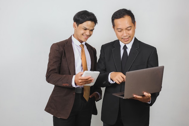 Dois empresários asiáticos de terno discutindo usando um laptop e um telefone inteligente