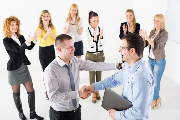 Dois empresários bem sucedidos apertando as mãos na reunião. Grupo de seu colega comemorando ao fundo.