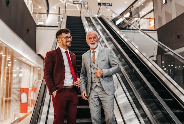 Dois empresários em frente a escada rolante e conversando.