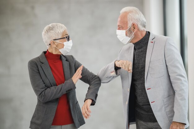 Dois empresários seniores cumprimentando com cotovelos em um escritório moderno durante a pandemia do vírus corona para evitar apertos de mão.