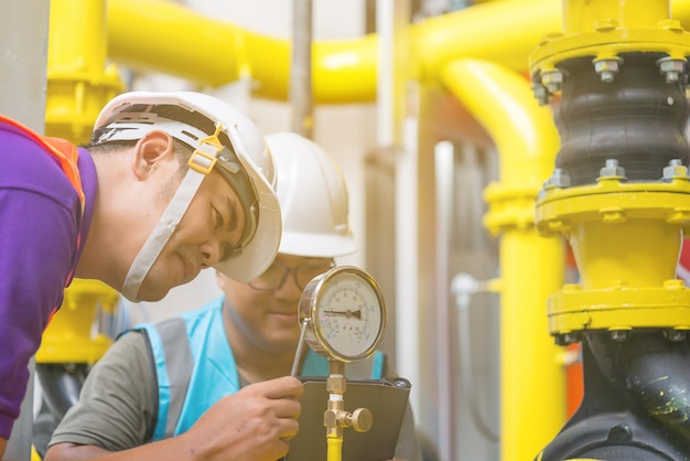 Dois engenheiros asiáticos trabalhando na manutenção da sala da caldeira verificando dados técnicos do equipamento do sistema de aquecimentoTailândiapessoasDiscutir a questão sobre a pressão do tubo