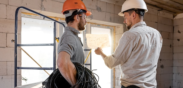 Dois engenheiros construtores conversando no canteiro de obras, um engenheiro explicando um desenho a um trabalhador.