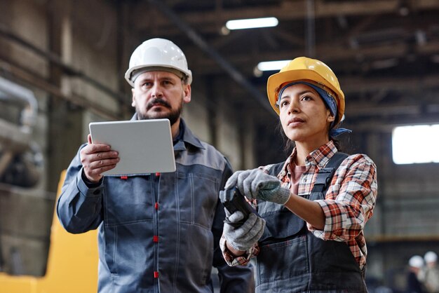 Dois engenheiros contemporâneos com tablet e controle remoto olhando para a máquina