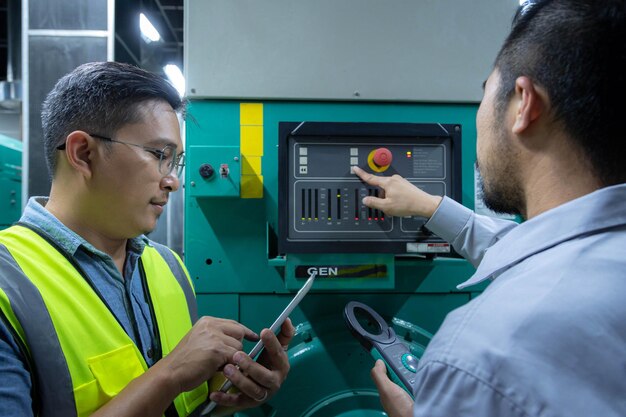 Dois engenheiros de fábrica usam driver de tablet com gerador automático na sala de máquinas, verifique o gerador com tablet.