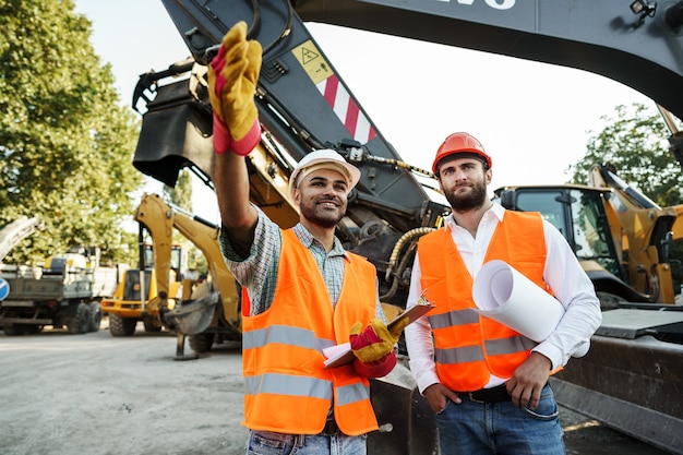 Foto dois engenheiros discutindo seu trabalho contra máquinas de construção