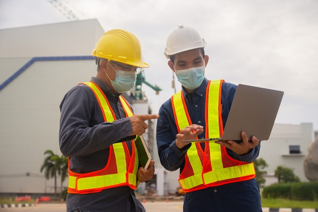 Dois engenheiros trabalhando com tecnologia de computador na construção do local, máscara de desgaste de dois engenheiros protege covid19