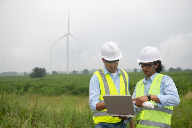 Dois engenheiros trabalhando e segurando o relatório na estação geradora de energia da fazenda de turbinas eólicas na montanhaTailândia