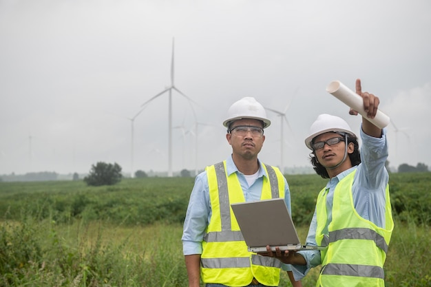 Dois engenheiros trabalhando e segurando o relatório na estação geradora de energia da fazenda de turbinas eólicas na montanhaTailândia