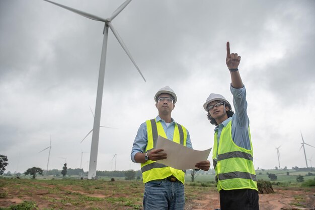 Dois engenheiros trabalhando e segurando o relatório na estação geradora de energia da fazenda de turbinas eólicas na montanhaTailândia