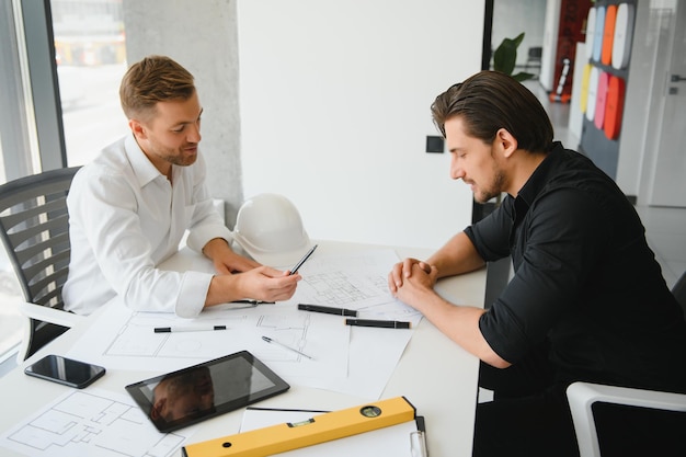 Dois engenheiros trabalhando juntos e usando tablet digital procurando planta e análise com plano arquitetônico na mesa