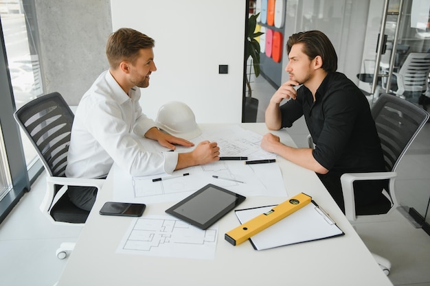 Foto dois engenheiros trabalhando juntos e usando tablet digital procurando planta e análise com plano arquitetônico na mesa