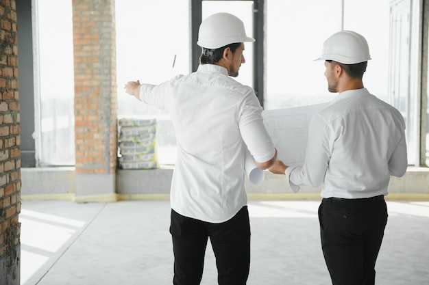 Dois especialistas inspecionam o projeto imobiliário do canteiro de obras do edifício industrial comercial com engenheiro civil