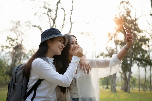 Dois estudantes asiáticos felizes usando um telefone inteligente tomam uma selfie durante o intervalo no campus da universidade.