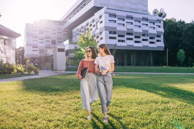 Dois estudantes felizes andam da universidade olhando um para o outro usando óculos segurando livros