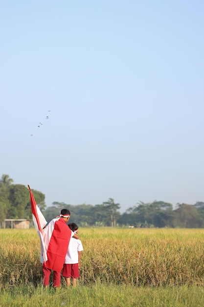 Dois estudantes indonésios segurando bandeiras durante o dia da independência no campo de arroz. primário orgulhoso