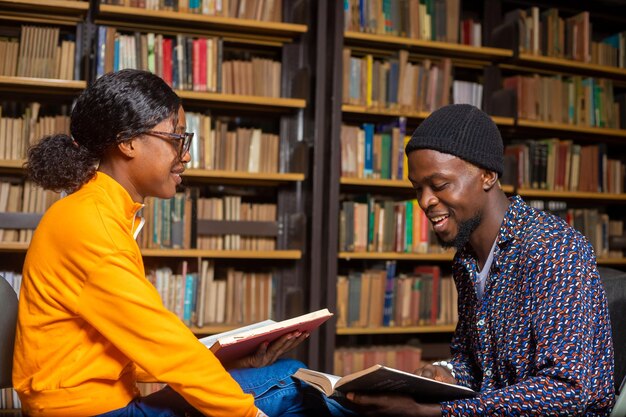 Dois estudantes inteligentes trabalhando em casa lendo livros atentamente sentados na mesa quadrada da biblioteca ao lado das estantes