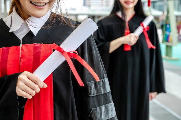 Dois estudantes universitários asiáticos usam vestidos com diploma de graduação