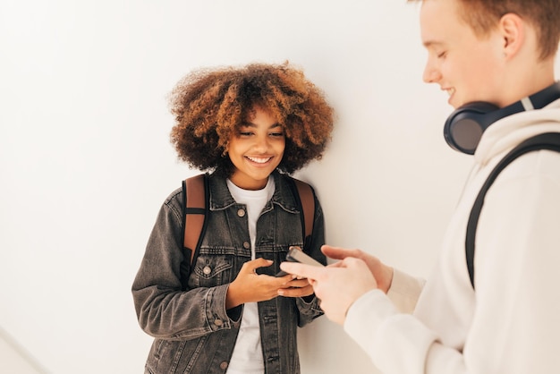 Dois estudantes universitários de pé juntos na parede olhando para seus smartphonesx9xA