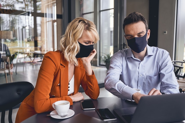 Dois executivos modernos focados em máscaras, sentados na mesa do escritório