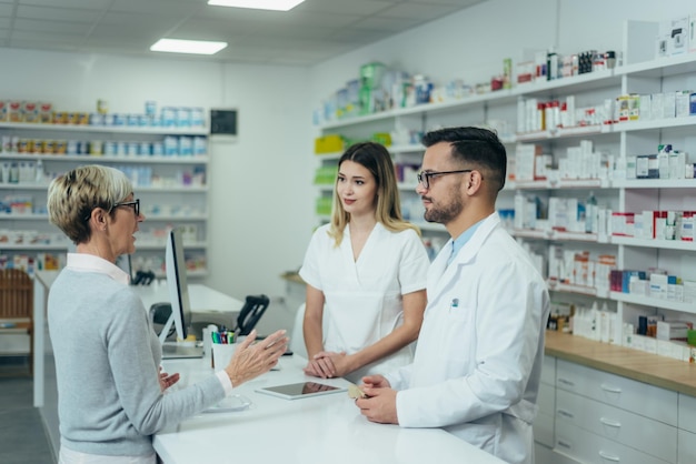 Dois farmacêuticos dando medicamentos prescritos para cliente sênior em uma farmácia