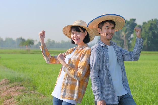 Dois fazendeiros asiáticos em pé e levantaram as mãos em uma fazenda de arroz verde. conceito de alguns fazendeiros.