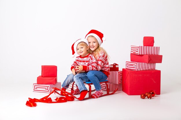 Dois filhos, um menino e uma menina com suéteres e chapéus, o Papai Noel está sentado em um trenó para carregar presentes. estúdio, fundo branco, espaço para texto