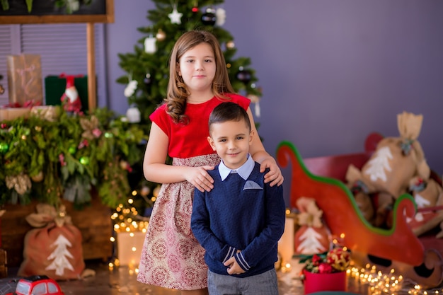 Dois filhos, uma menina e um menino perto de uma árvore de natal
