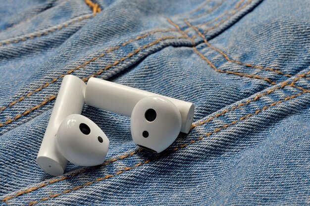 Dois fones de ouvido sem fio brancos repousam sobre o jeans. fechar-se.