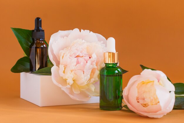 Dois frascos com soro natural artesanal e uma flor de peônia em fundo bege. auto-cuidado com cosméticos orgânicos feitos à mão.