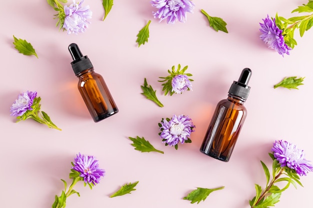 Dois frascos conta-gotas de vidro para uso cosmético e flores roxas em um fundo roxo prevenção de mudanças de pele relacionadas à idade vista superior